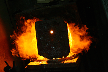 Glowing furnace opening with molten glass batch inside, flames on both sides