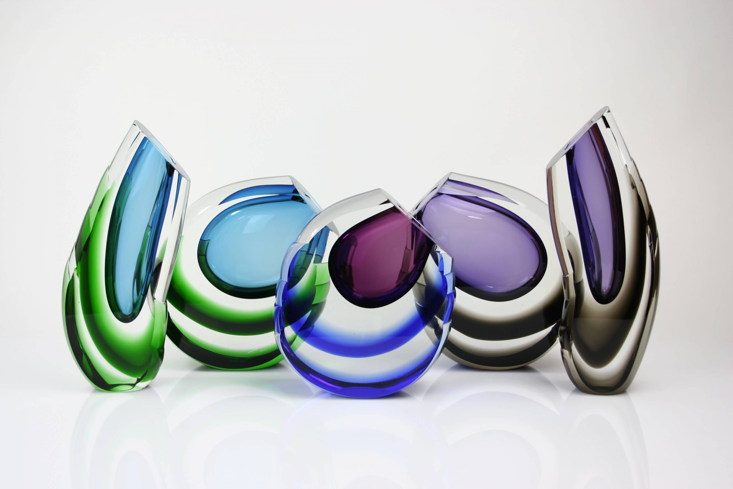 Row of hand blown Ozzaro glass vessels in blue, green, amethyst and smoked crystal
